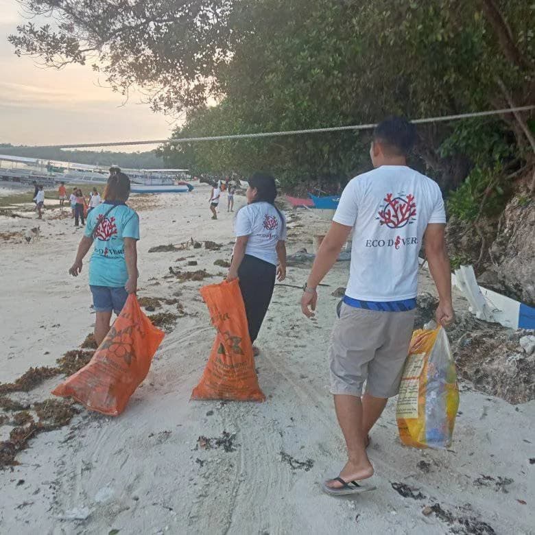 Eco Divers staff carrying bags of collected trash during a beach cleanup